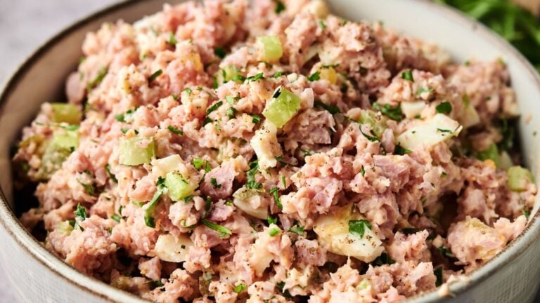 A bowl filled with ham salad containing chopped ham, celery, mayonnaise, eggs, and herbs, garnished with black pepper.