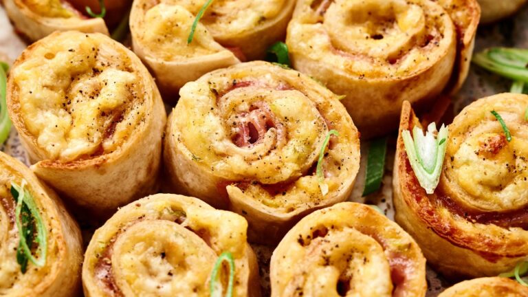 Close-up of baked pinwheel snacks filled with melted cheese and ham, sprinkled with black pepper and garnished with chopped green onions.