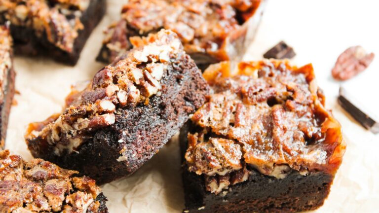 Close-up of several pecan brownies with a rich, fudgy base and a pecan topping, arranged on parchment paper.