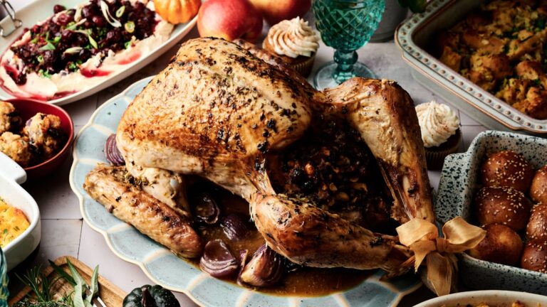 A roasted turkey stuffed with vegetables is served on a platter, surrounded by various side dishes and desserts on a festive table.