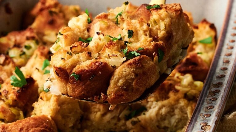 A close-up of a serving of bread stuffing with herbs, scooped from a baking dish.