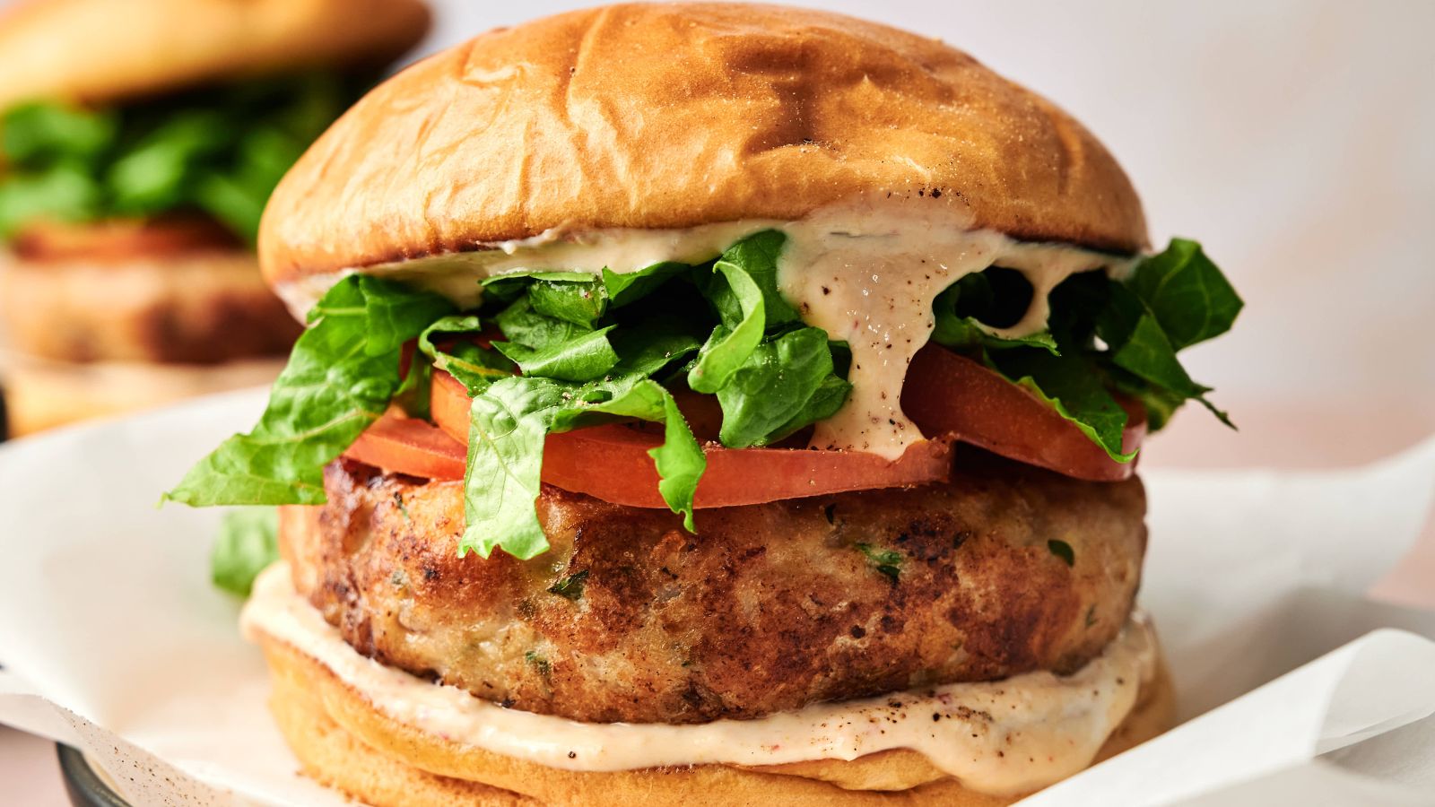 A close-up of a chicken burger with lettuce, tomato, and a creamy sauce in a toasted bun.