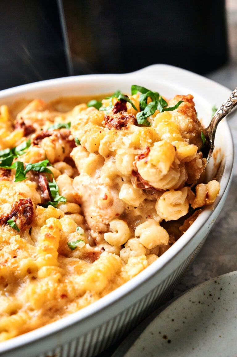 A close-up of baked macaroni and cheese with sun-dried tomatoes served in a white casserole dish, inspired by the flavors of Air Fryer Marry Me Chicken Casserole and topped with chopped fresh herbs.