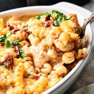 A close-up of baked macaroni and cheese with sun-dried tomatoes served in a white casserole dish, inspired by the flavors of Air Fryer Marry Me Chicken Casserole and topped with chopped fresh herbs.