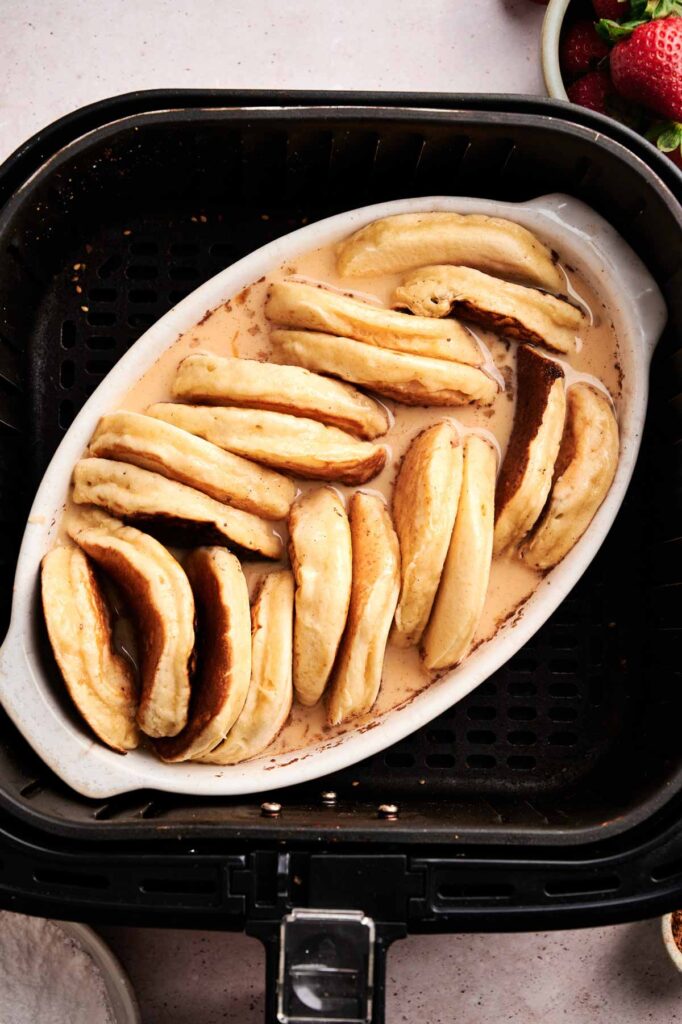 A white oval dish filled with stacked Air Fryer Pancake Casserole in a creamy sauce, placed inside an air fryer basket.