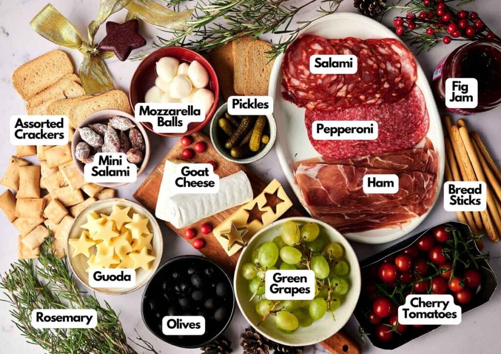 A Christmas Tree Charcuterie Board with labeled sections for assorted crackers, mini salami, gouda, rosemary, mozzarella balls, olives, goat cheese, pickles, grapes, salami, pepperoni, ham, fig jam, bread sticks, and cherry tomatoes.