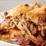 A close-up of a serving of Air Fryer Chicken Cordon Bleu Casserole with shredded meat and a golden breadcrumb topping being lifted from a white dish.