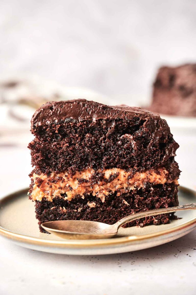 A slice of layered chocolate cake with a creamy filling on a plate, accompanied by a spoon.