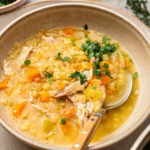 A bowl of Italian Penicillin Soup with shredded chicken, diced carrots, celery, and herbs, with a spoon resting inside the bowl.