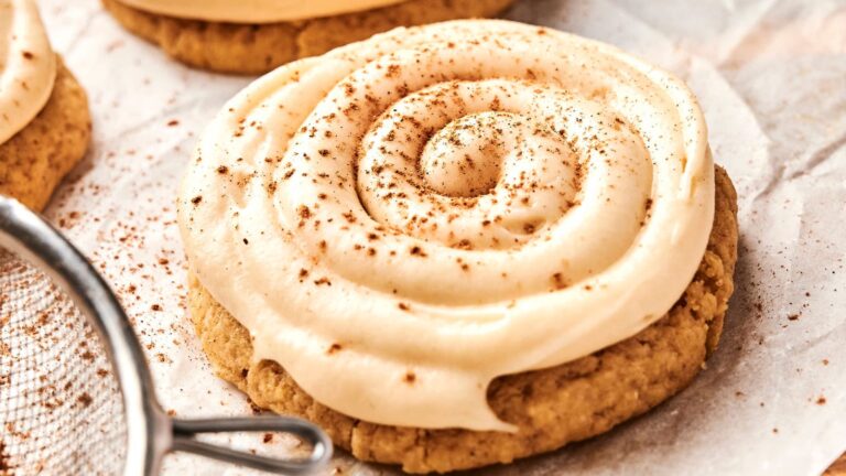 A close-up of a frosted cookie with a spiral of creamy icing and a light dusting of brown spice, placed on parchment paper.
