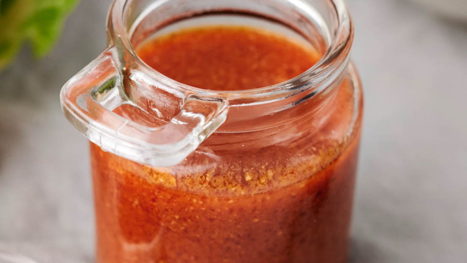 A small glass jar filled with reddish-brown sauce or dressing, sitting on a light surface.