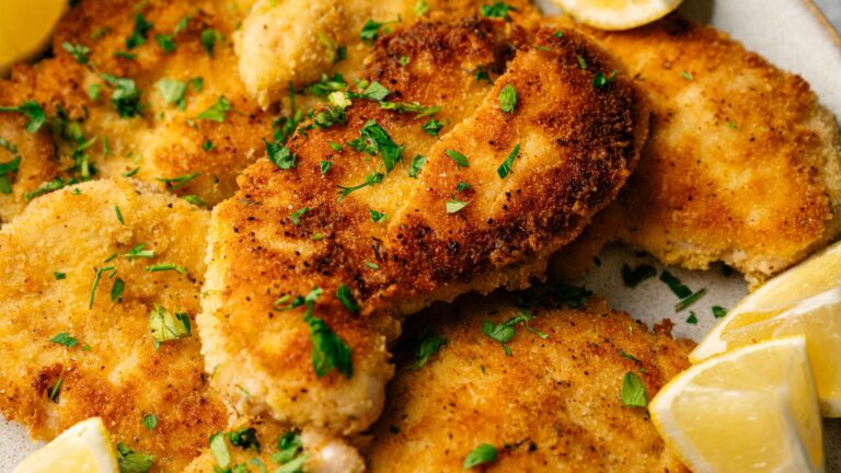 Golden-brown breaded chicken cutlets garnished with chopped parsley, served with lemon wedges on the side.