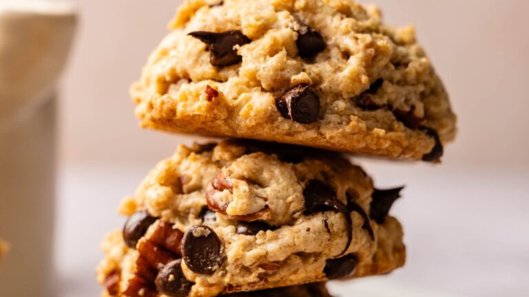 Two thick chocolate chip cookies with visible nuts are stacked on top of each other against a neutral background.