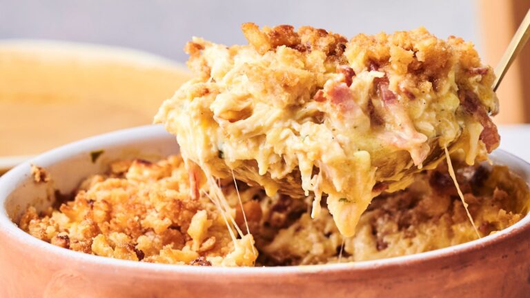 A spoon lifts a cheesy, breadcrumb-topped casserole from a baking dish, showing a creamy and textured filling.
