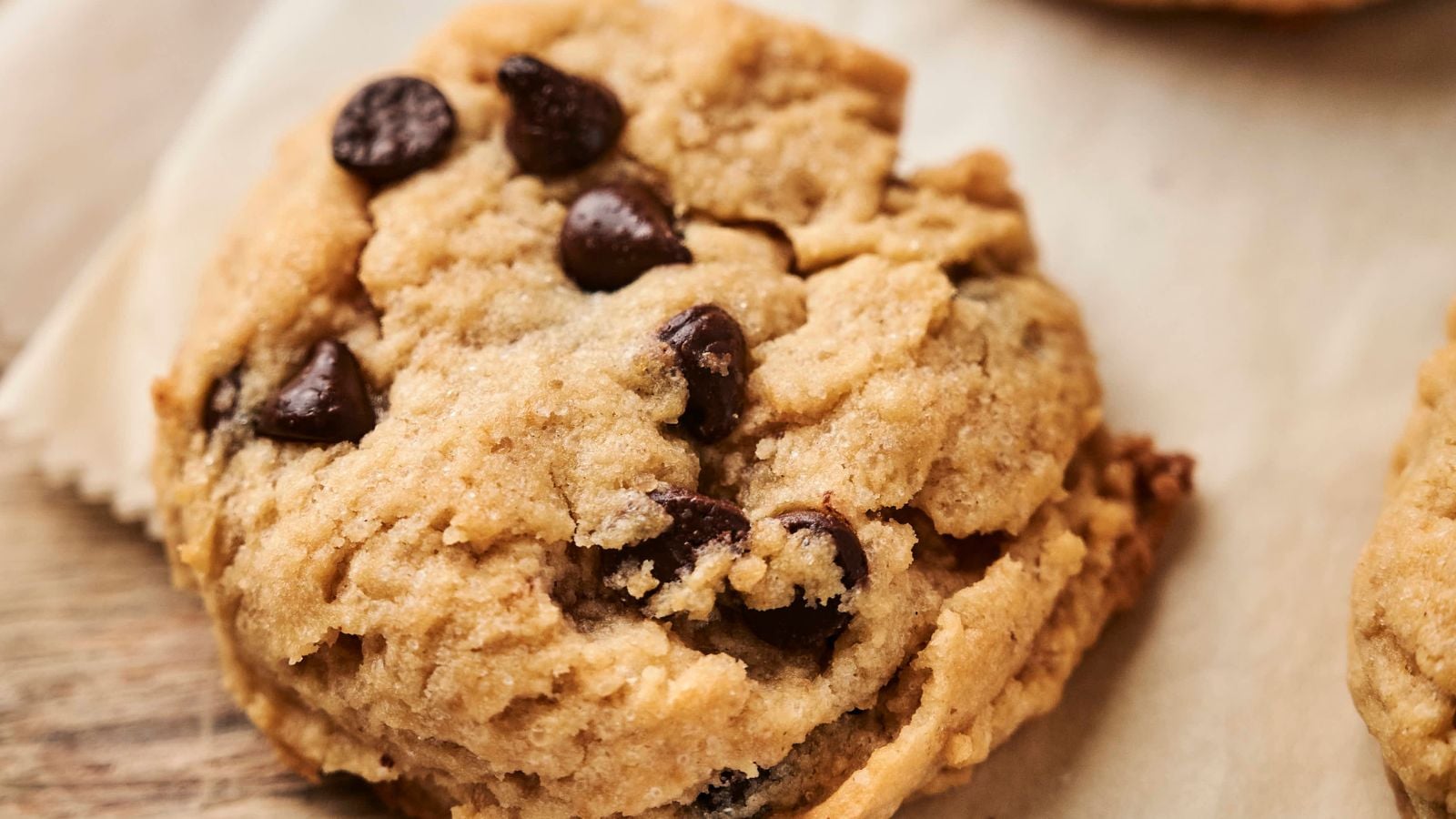 A close-up of a vegan chocolate chip cookie on a piece of parchment paper, showcasing its delightful texture and rich chocolate chips.
