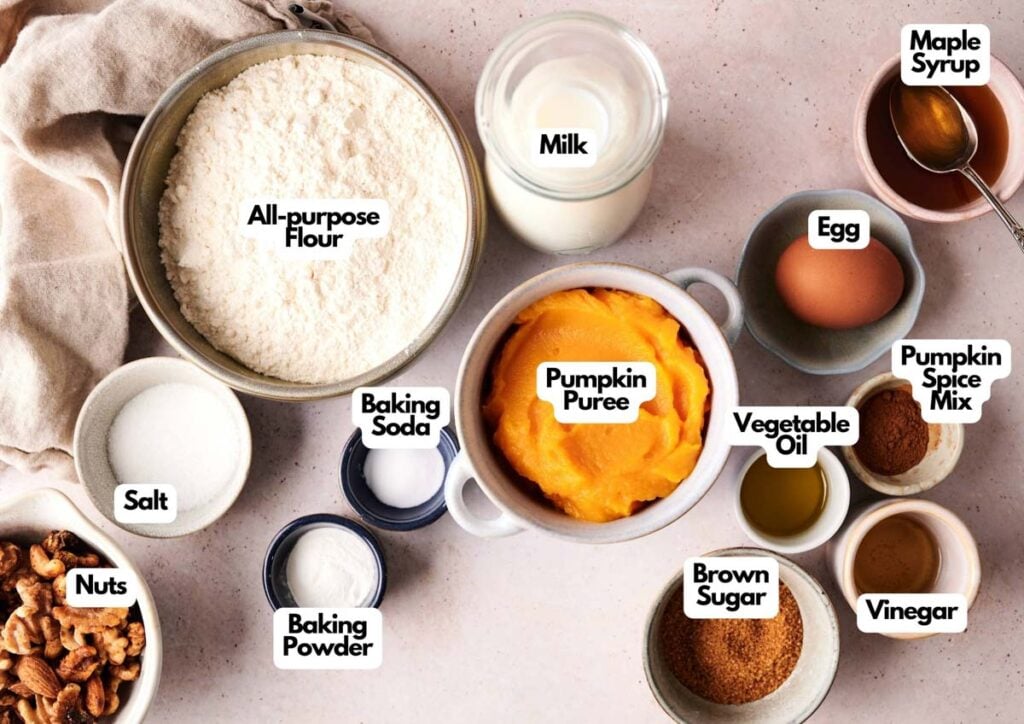 Assorted baking ingredients for Air Fryer Pumpkin Pancake&mdash;flour, pumpkin puree, milk, egg, brown sugar, nuts, and labeled spices&mdash;are arranged on a light surface.