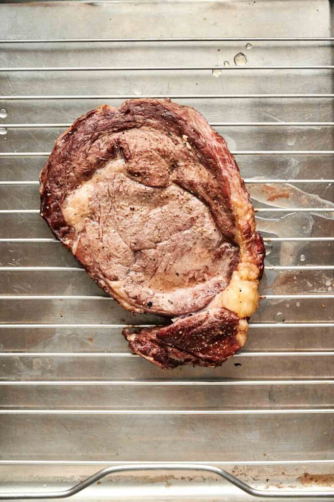 A perfectly cooked reverse sear steak rests on a metal wire rack over a baking tray.