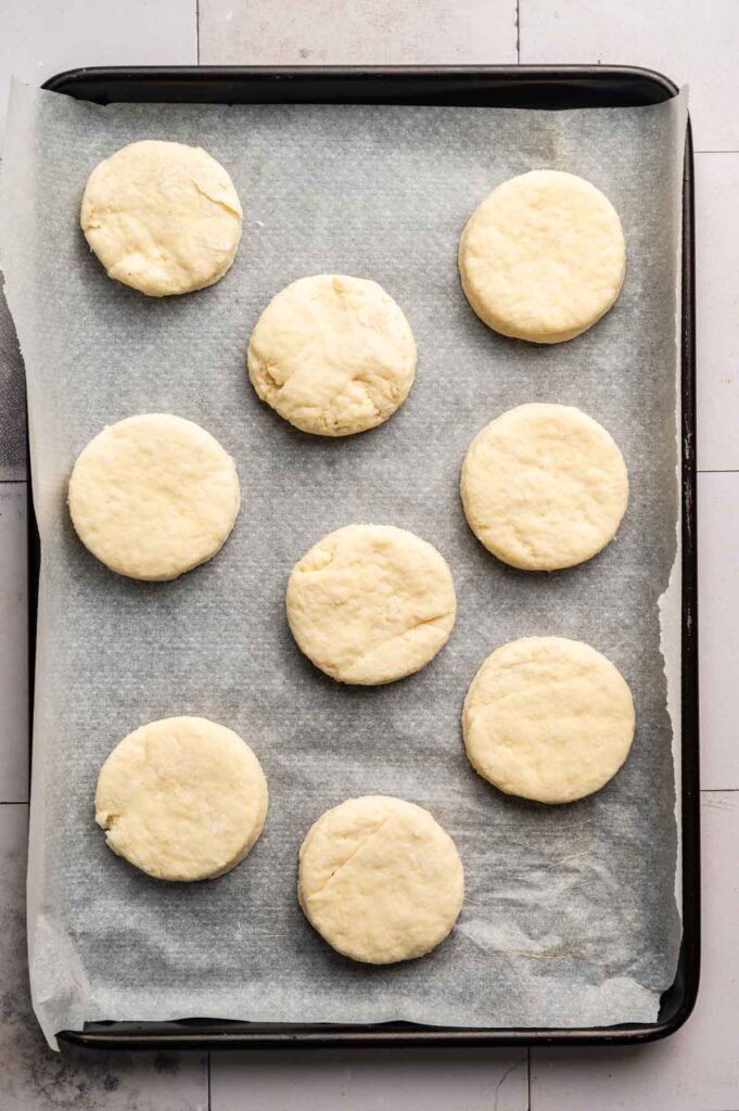 Ten unbaked Sourdough Biscuit dough rounds arranged on a parchment-lined baking sheet.