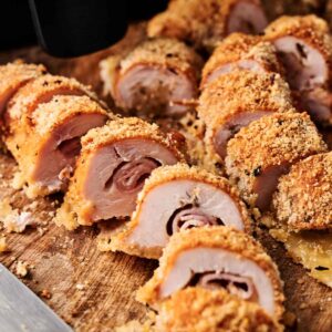 Air Fryer Chicken Cordon Bleu sliced to reveal layers of ham and cheese inside its crispy breaded coating, beautifully arranged on a wooden cutting board.