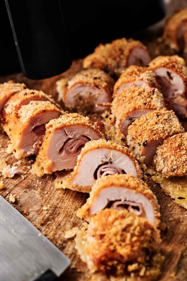 Air Fryer Chicken Cordon Bleu sliced to reveal layers of ham and cheese inside its crispy breaded coating, beautifully arranged on a wooden cutting board.