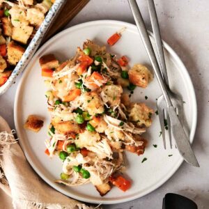 A plate of Air Fryer Chicken and Stuffing Casserole featuring bread cubes, peas, and diced carrots, served with a fork and knife on a white surface.