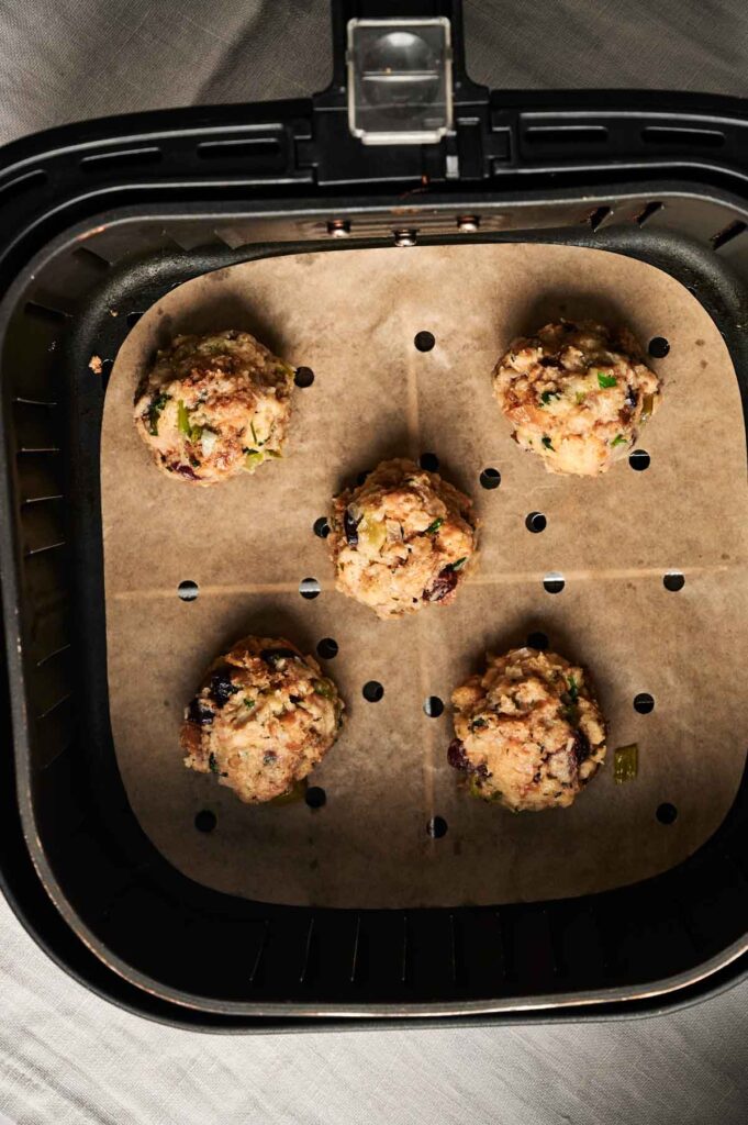 Five uncooked Air Fryer Stuffing Balls are arranged on parchment paper inside an air fryer basket, ready to be perfectly crisped.