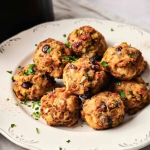 A white plate with eight Air Fryer Stuffing Balls garnished with chopped parsley, set on a light-colored tablecloth.