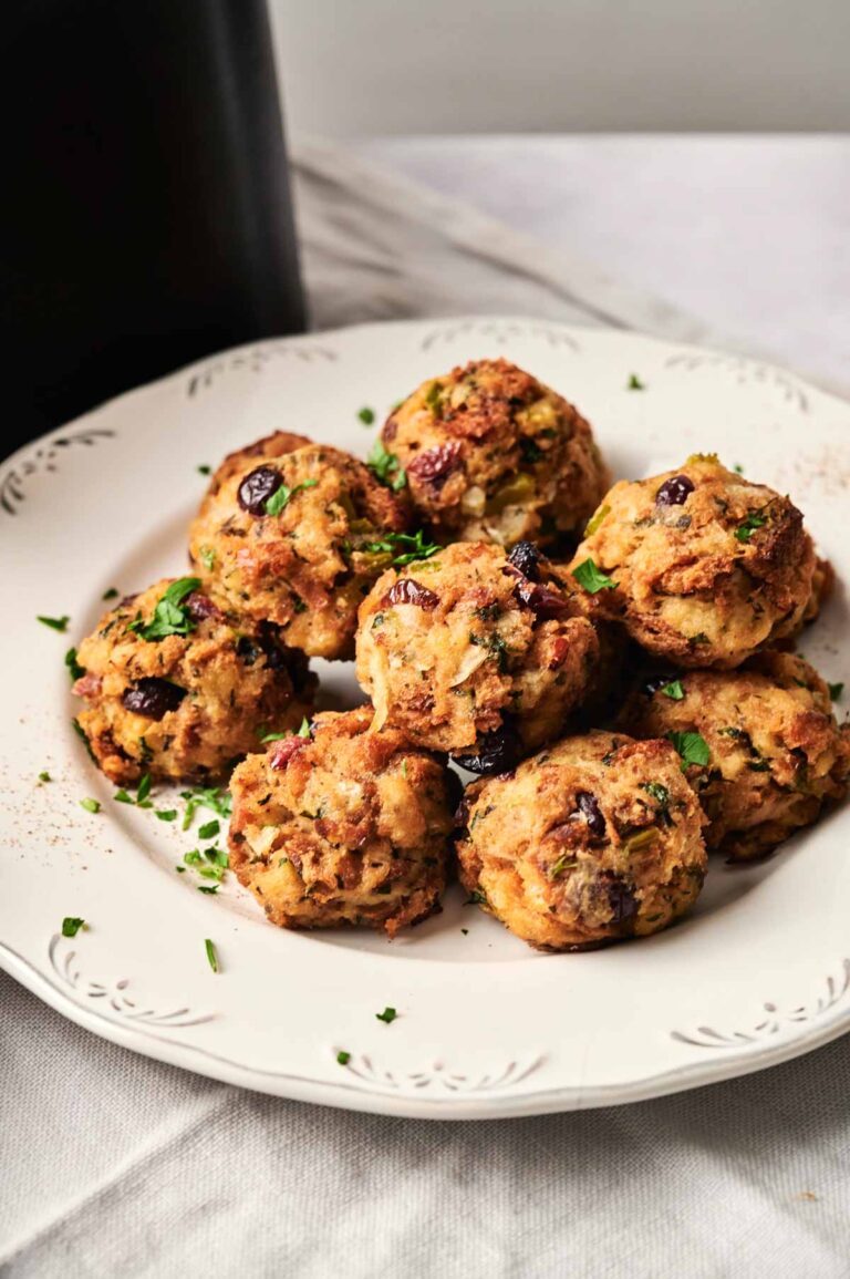 A white plate with eight Air Fryer Stuffing Balls garnished with chopped parsley, set on a light-colored tablecloth.