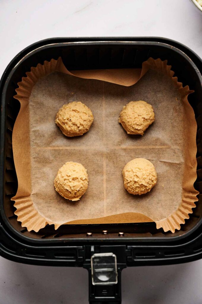 Four unbaked Air Fryer Tiramisu Cookies dough balls rest on parchment paper inside an air fryer basket.