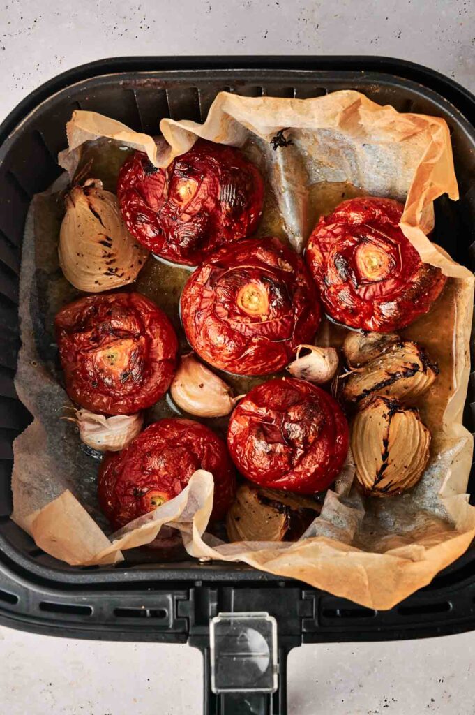 Roasted tomatoes, onions, and garlic on parchment paper inside an air fryer basket—perfect for making rich and flavorful Air Fryer Tomato Soup.