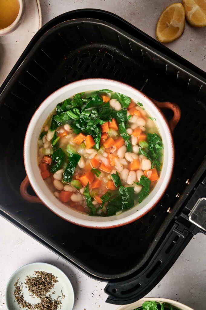 A bowl of Air Fryer White Bean Soup with spinach, carrots, and white beans cooking together for a hearty and healthy meal.