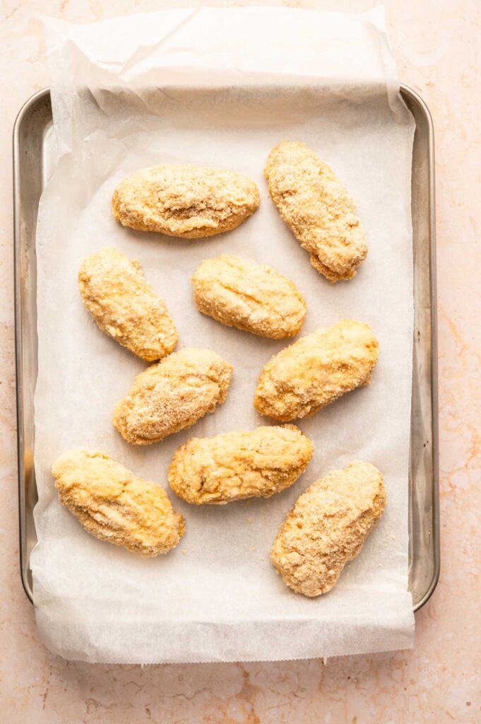 Nine breaded, oval-shaped chicken croquettes are arranged on a baking tray lined with parchment paper.