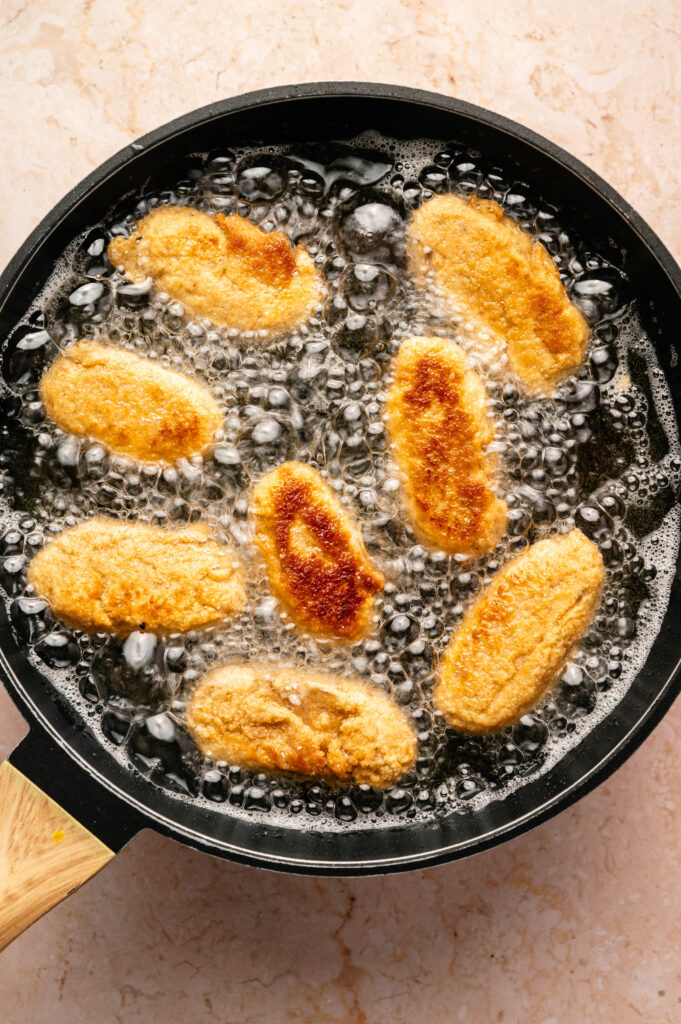 Chicken Croquettes frying in hot oil in a black pan, with bubbles forming around the golden-brown pieces.