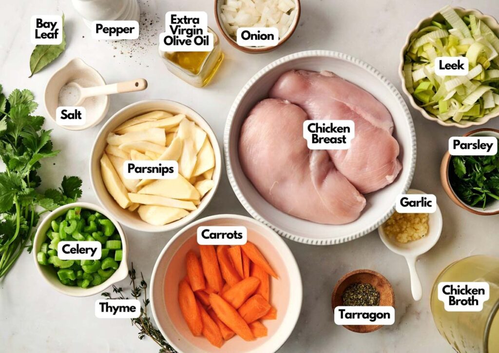 A variety of labeled ingredients for Air Fryer Chicken Soup are arranged on a countertop, including chicken breast, vegetables, herbs, spices, and olive oil.