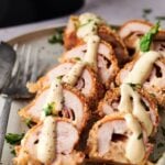 Sliced Air Fryer Chicken Cordon Bleu rolls topped with creamy sauce and chopped herbs, served on a plate with a fork and knife.