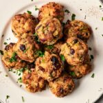 A plate of round Air Fryer Stuffing Balls garnished with chopped parsley, featuring visible pieces of herbs and dried cranberries.
