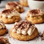 Close-up of Air Fryer Tiramisu Cookies topped with cocoa powder on a parchment-lined surface, with a white bowl in the background.
