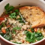 A bowl of Air Fryer White Bean Soup topped with fresh herbs and parsley, served with a slice of toasted bread.