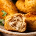 Close-up of delicious Chicken Croquettes, breaded and fried to perfection, broken open to reveal a creamy shredded chicken filling, served on a plate with parsley garnish.