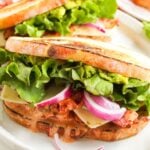 Close-up of a Chipotle Chicken Club sandwich with toasted bread, lettuce, sliced red onion, cheese, guacamole, and a creamy filling on a white plate.