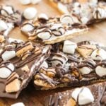 Loaded S'mores Bark topped with mini marshmallows, graham cracker pieces, and a rich chocolate drizzle sits on a wooden surface.