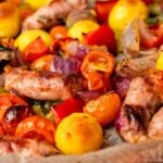 Sheet Pan Gnocchi, roasted sausages, cherry tomatoes, potatoes, red onions, and bell peppers on a baking tray.