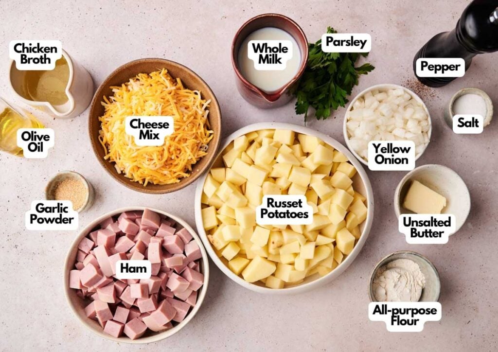 Top-down view of labeled ingredients for Air Fryer Ham and Potato Casserole, with russet potatoes, ham, cheese mix, yellow onion, parsley, and seasonings arranged on a light surface.