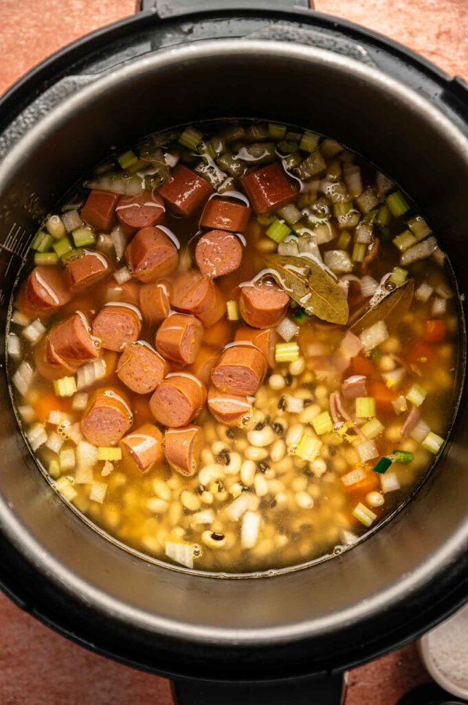 Chopped sausages, beans, vegetables, and broth in an Instant Pot create a delicious twist on Hoppin' John, ready to cook.