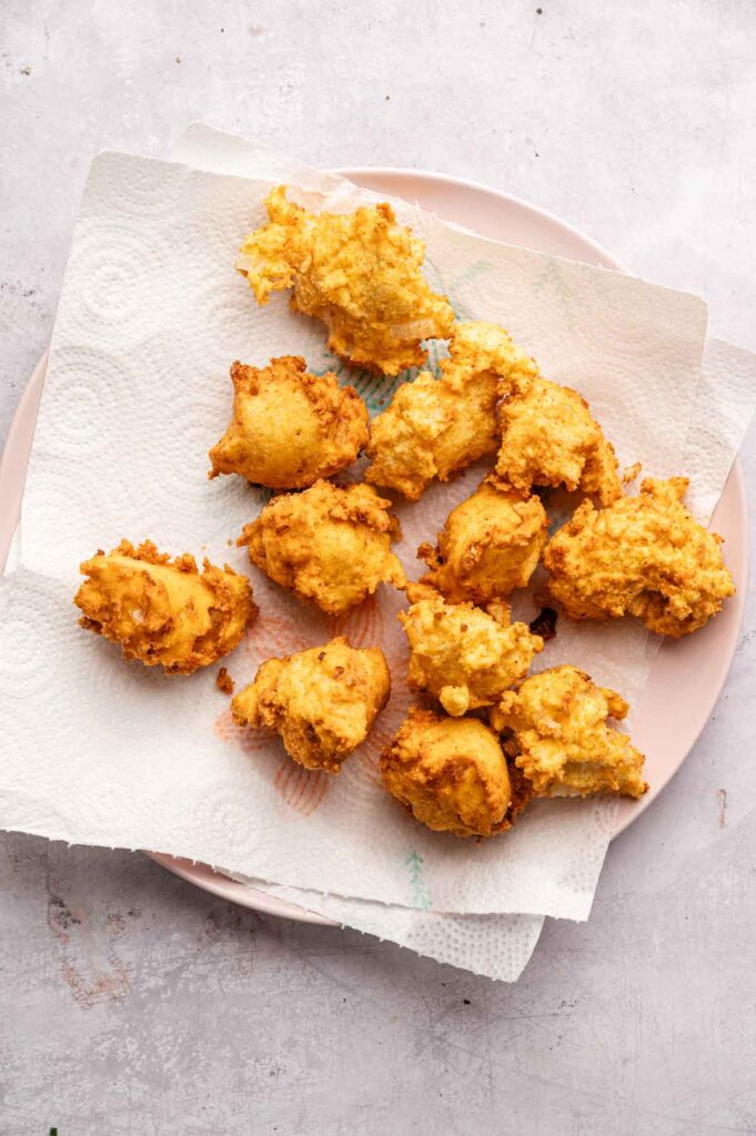 A plate lined with paper towels holds several golden-brown Hush Puppies, showcasing their crispy texture on a light background.
