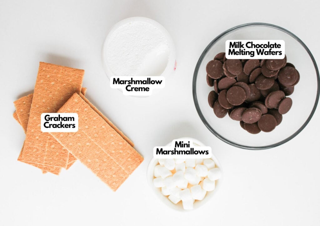 Four ingredients—graham crackers, marshmallow creme, milk chocolate melting wafers, and mini marshmallows—are arranged separately on a white surface, ready to be transformed into Loaded S'mores Bark.