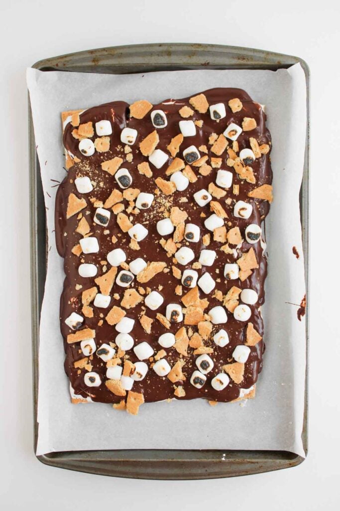 A baking sheet with Loaded S'mores Bark—a rectangular dessert topped with chocolate, mini marshmallows, and crushed graham crackers on parchment paper.