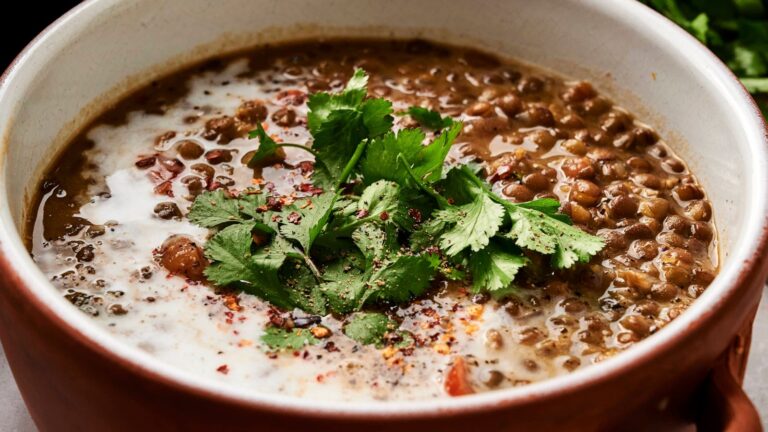A bowl of lentil soup topped with fresh cilantro, ground pepper, and a swirl of cream.