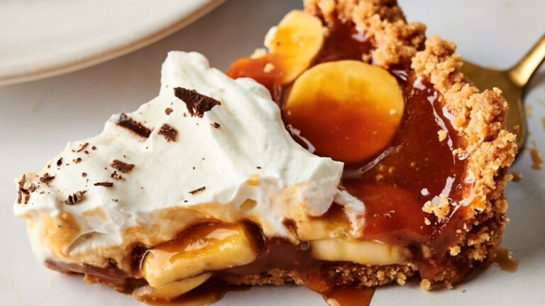 A slice of banoffee pie with a graham cracker crust, banana slices, caramel sauce, whipped cream, and chocolate shavings on a plate.