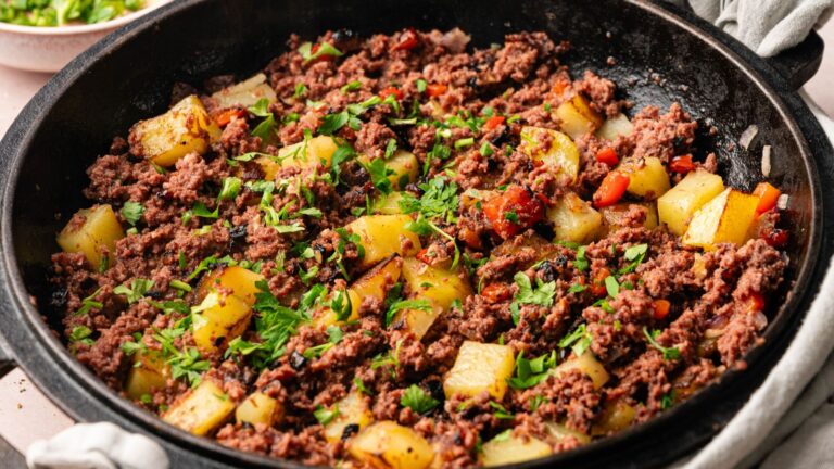 A skillet filled with cooked ground beef, diced potatoes, and red peppers, garnished with chopped fresh parsley.